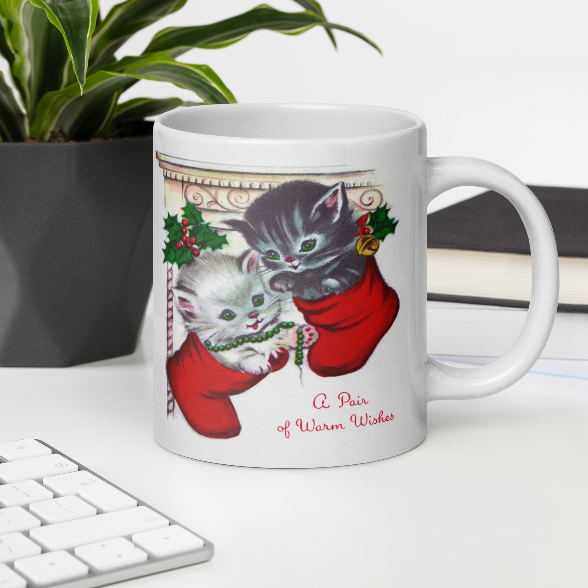 This white ceramic glossy coffee mug features two adorable kittens in red stockings at a Christmas mantle. The print is retro kitsch and says A Pair of Warm Wishes.